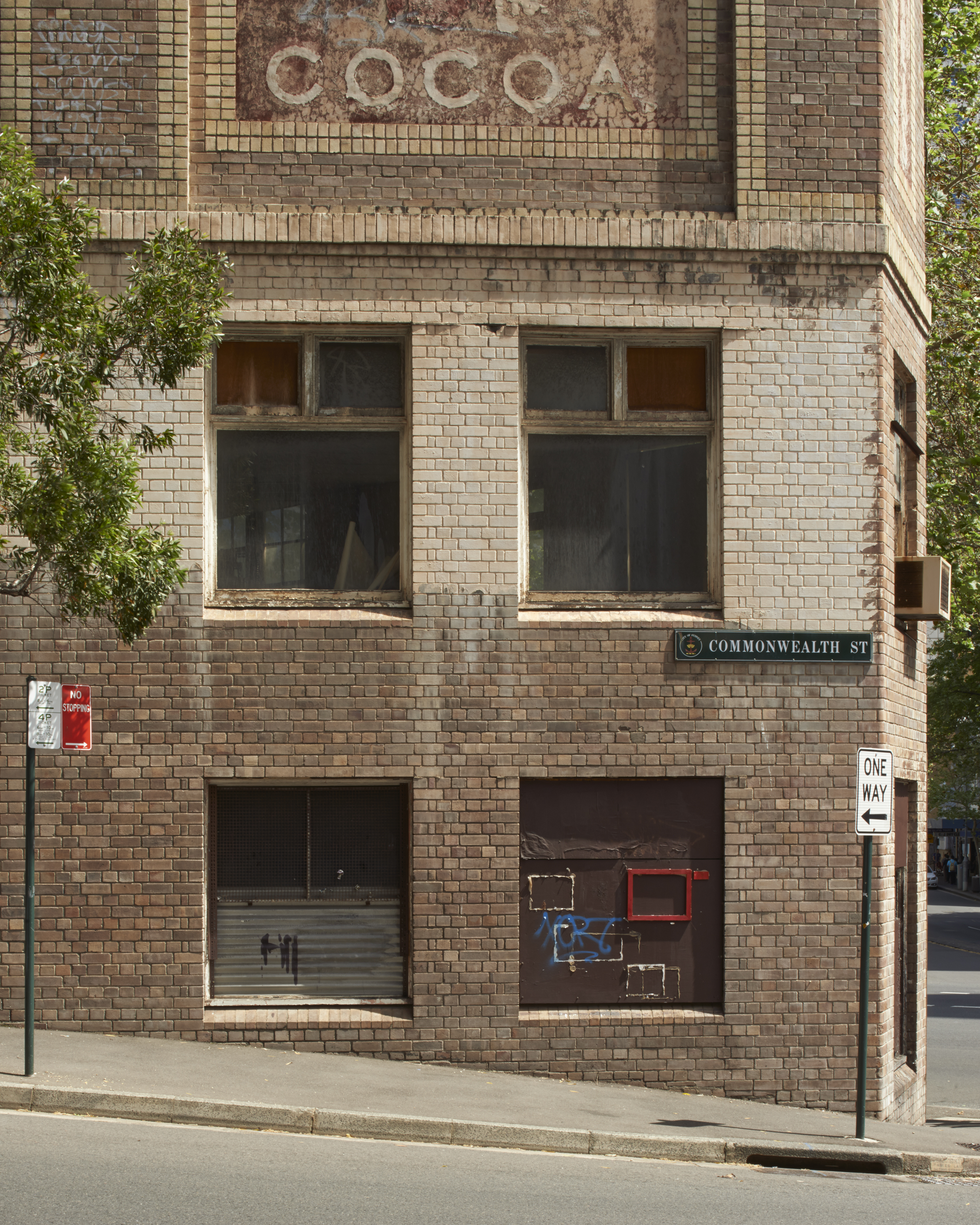 An old brick building corner with weathered paint, street signs, and windows in an urban environment on a sunny day.