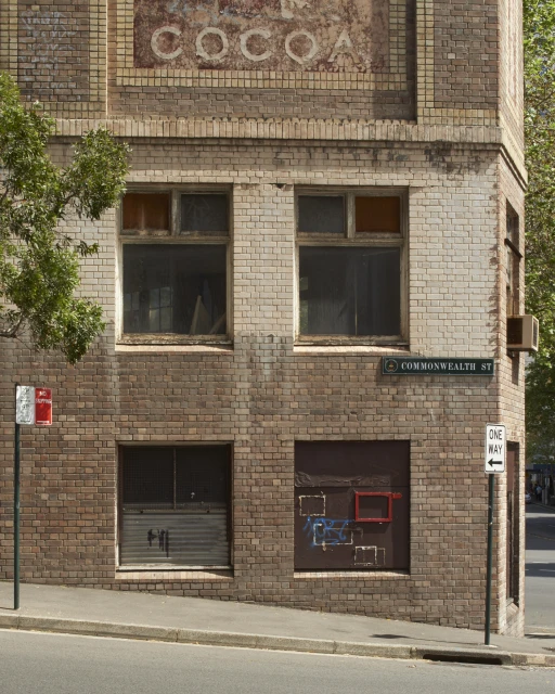 An old brick building corner with weathered paint, street signs, and windows in an urban environment on a sunny day.