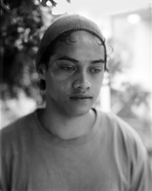 Black and white portrait of a young adult with a thoughtful expression wearing a beanie, captured with soft lighting and shallow depth of field.