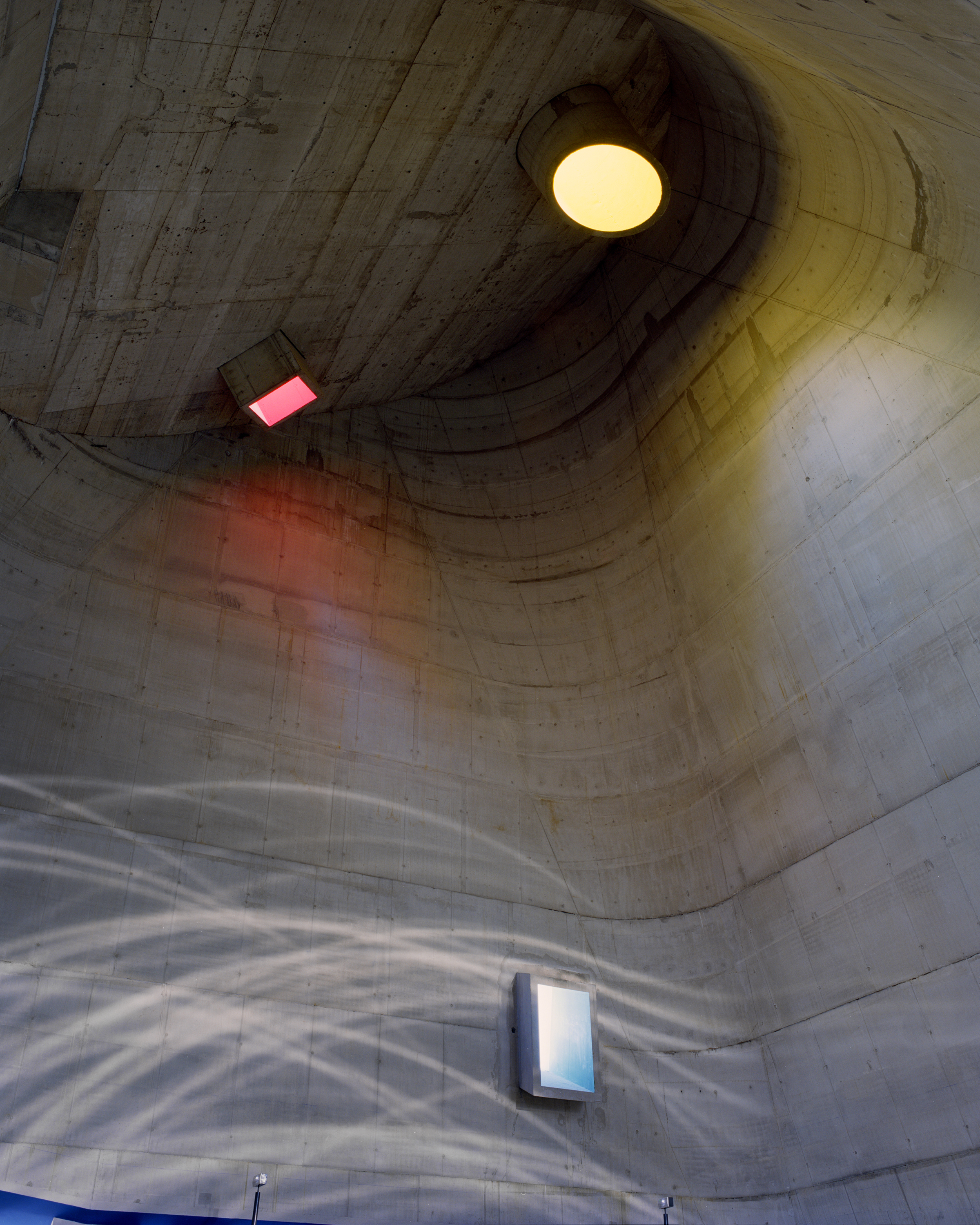 Interior view of a concrete structure with a curved ceiling, illuminated by a mix of natural and artificial light, and water reflections.