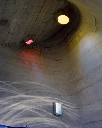 Interior view of a concrete structure with a curved ceiling, illuminated by a mix of natural and artificial light, and water reflections.