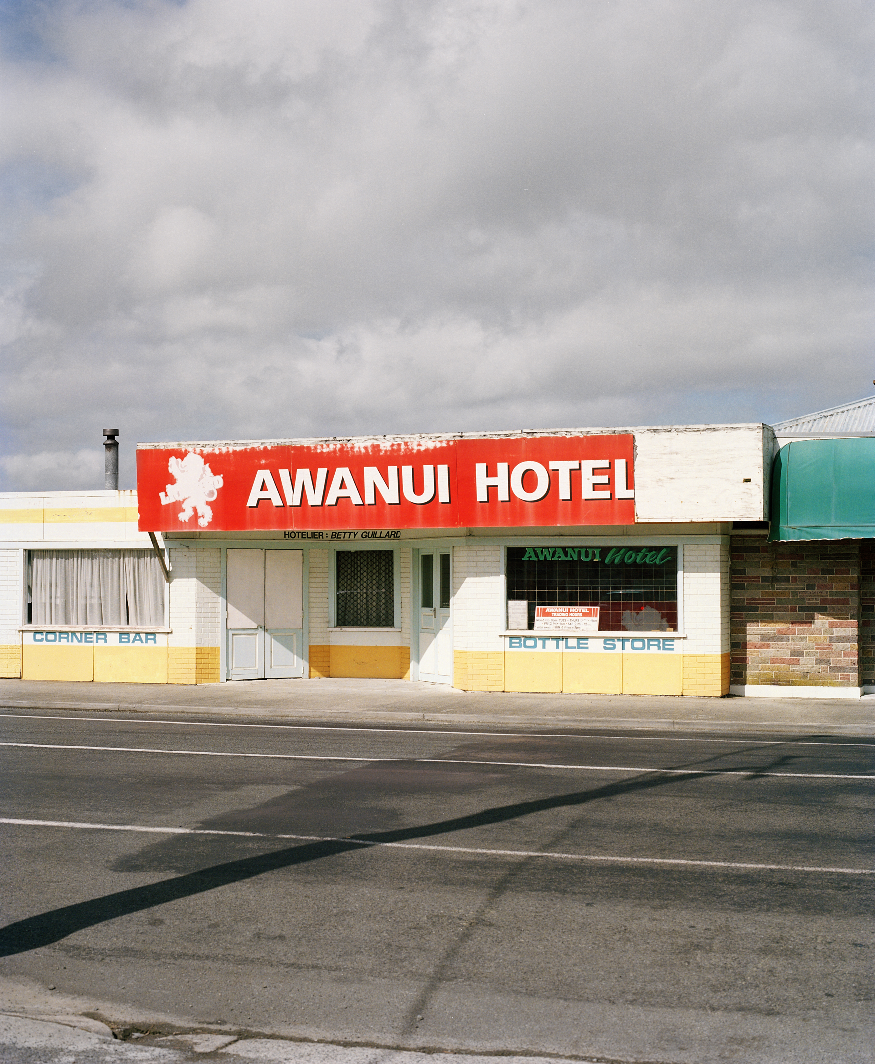Exterior view of the Awanui Hotel, featuring a red sign against the building, and an empty road in front on a cloudy day.