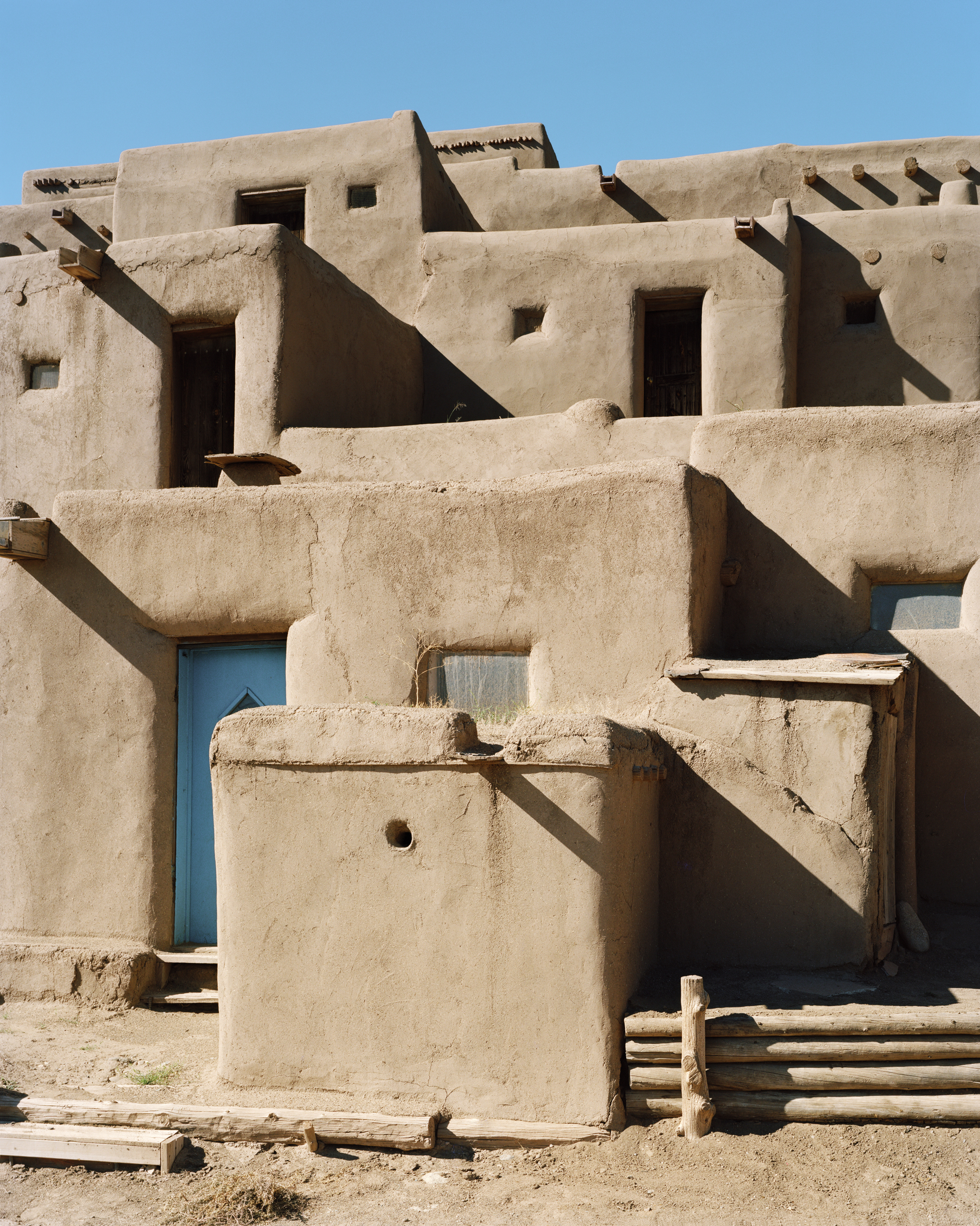 Adobe architecture with tan adobe walls and blue door under a blue sky. Southwestern architectural style with geometric shapes and textures.