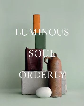Still life with ceramic objects, arranged in a tower, including blocks, a vase and an egg, against a light green backdrop.