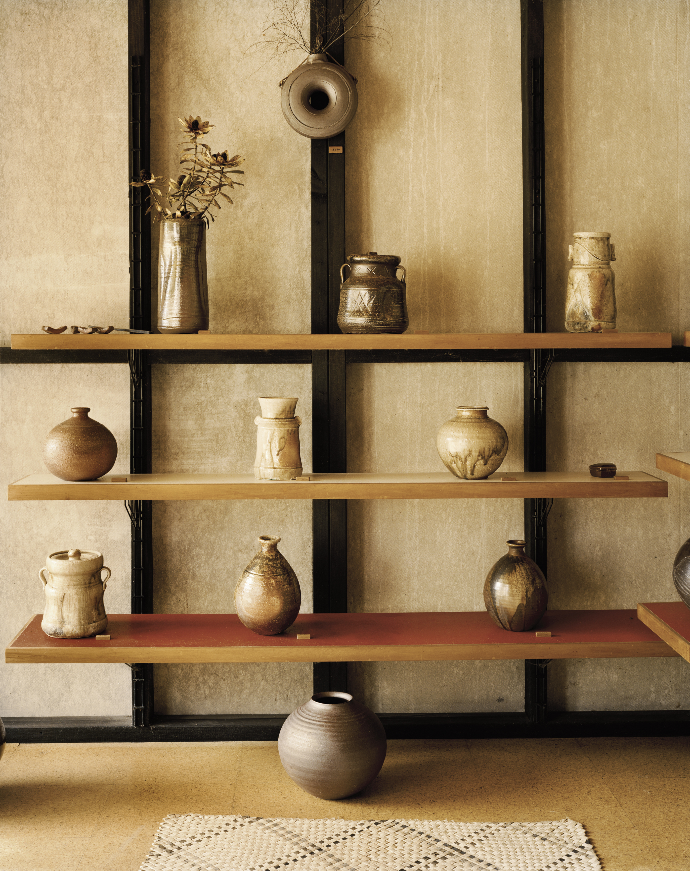 Still life of various ceramic vases and jars on a tiered shelf against a textured wall, featuring neutral tones and clean lines.