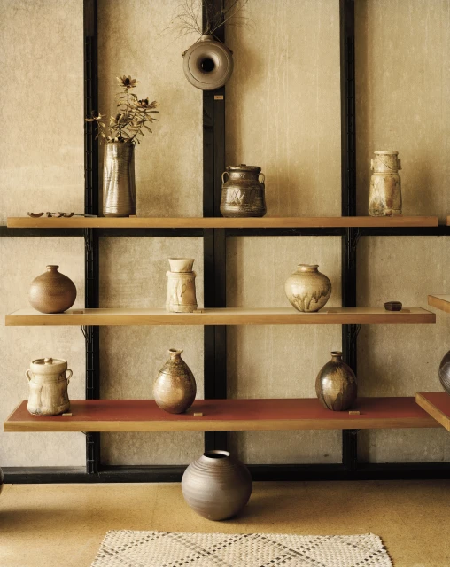 Still life of various ceramic vases and jars on a tiered shelf against a textured wall, featuring neutral tones and clean lines.