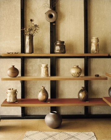 Still life of various ceramic vases and jars on a tiered shelf against a textured wall, featuring neutral tones and clean lines.
