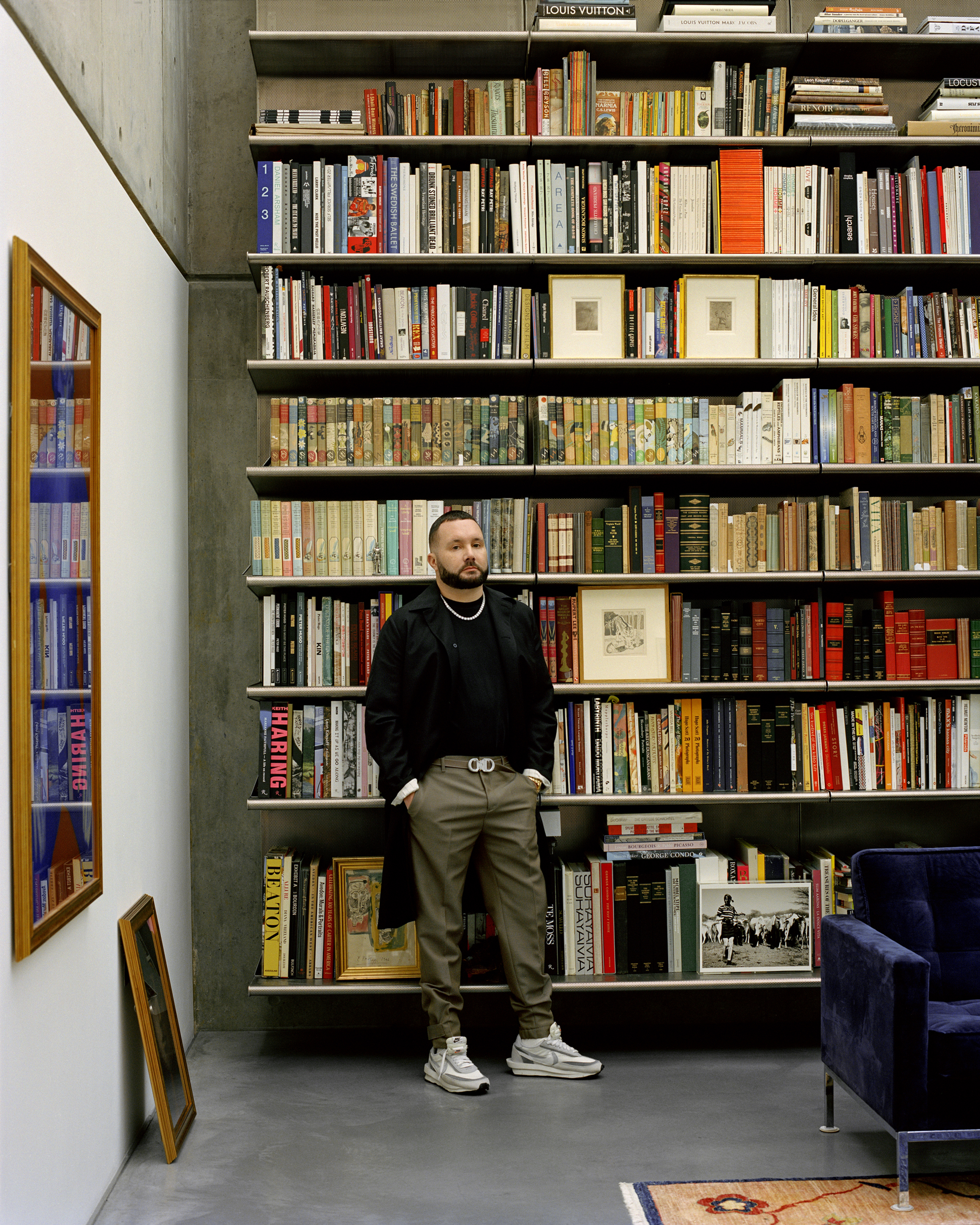 Man standing in front of a tall, fully stocked floor-to-ceiling bookshelf in a modern room, photographed by Derek Henderson