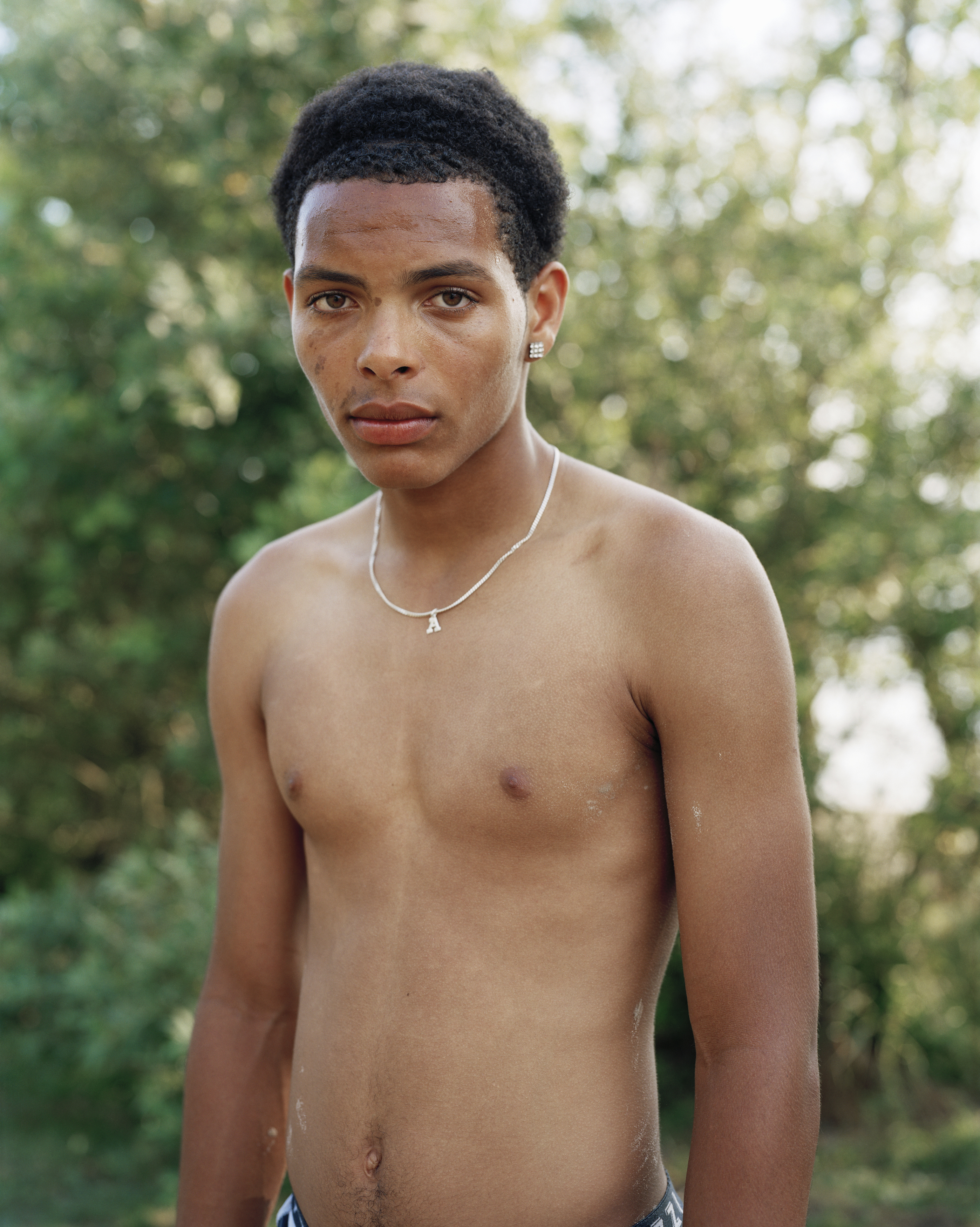 Portrait of a young man with short dark hair wearing a silver chain necklace in Sydney, captured by Derek Henderson.