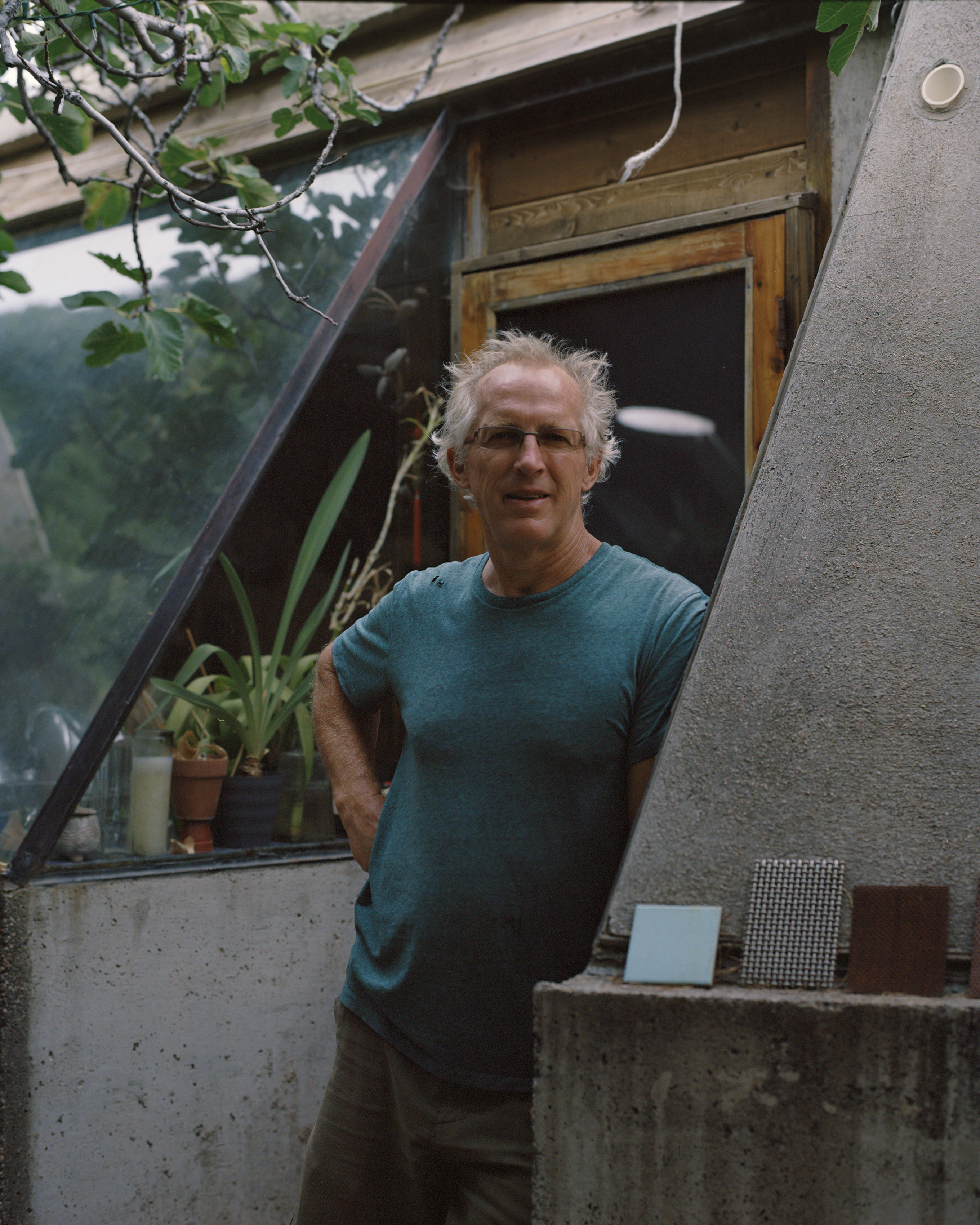 Man standing next to a modern concrete structure with various tiles displayed in front, amidst lush greenery and natural light.