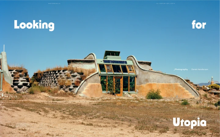 View of an earth house with a glass facade in a desert landscape under a clear blue sky on a sunny day. Solar panels are on the roof.