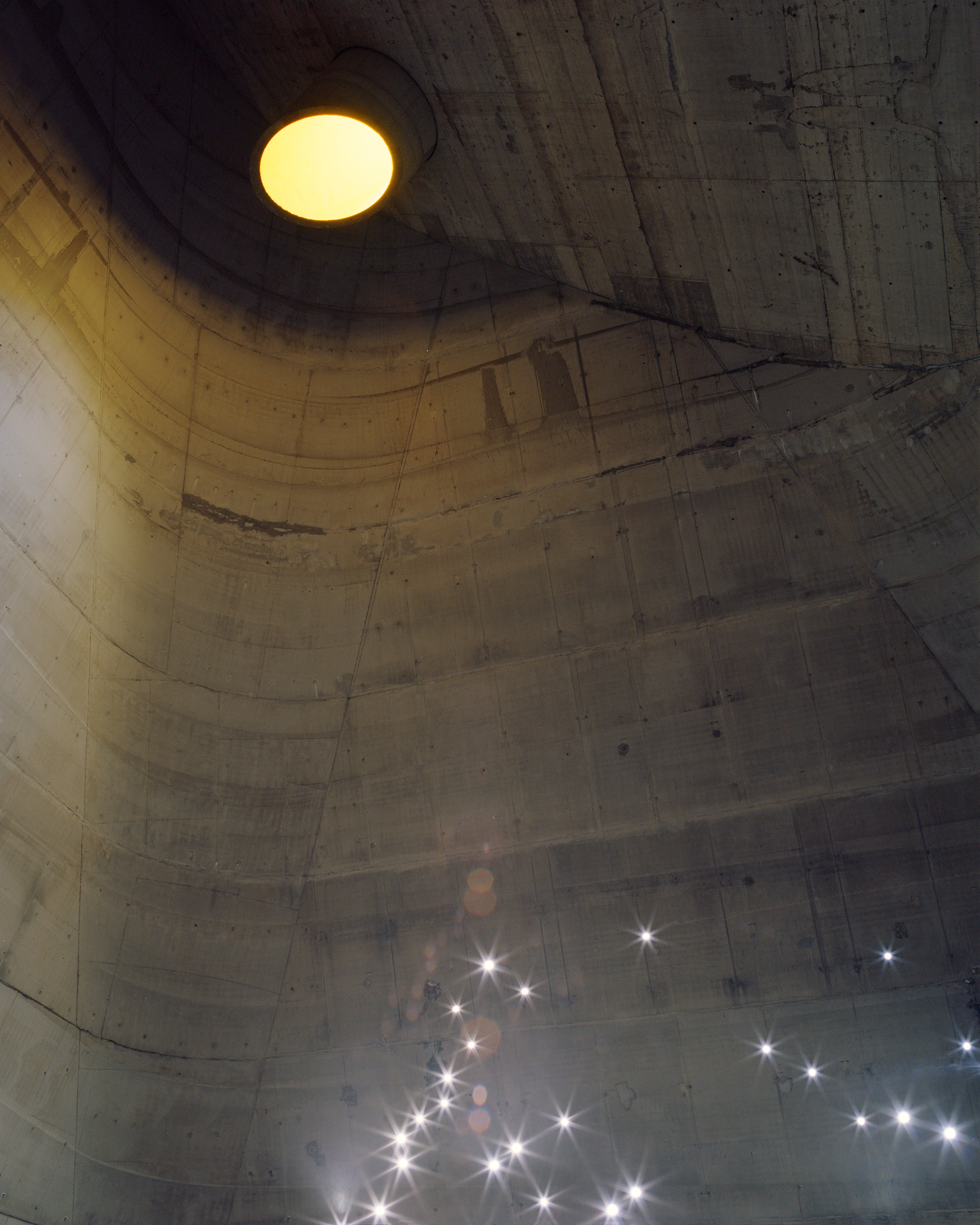 Architectural shot of a concrete dome ceiling with a central round light fixture, complemented by small, star-like lights below.