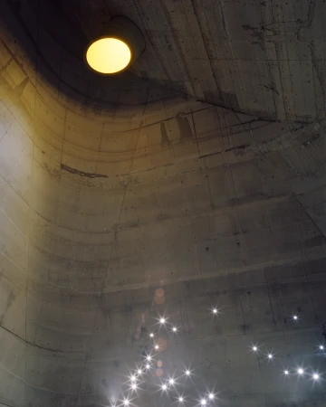 Architectural shot of a concrete dome ceiling with a central round light fixture, complemented by small, star-like lights below.