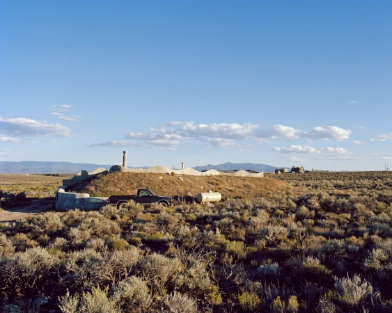 Exterior daytime shot of a black pick-up truck parked in front of an earth berm house in a rural, grassy field under a blue sky.