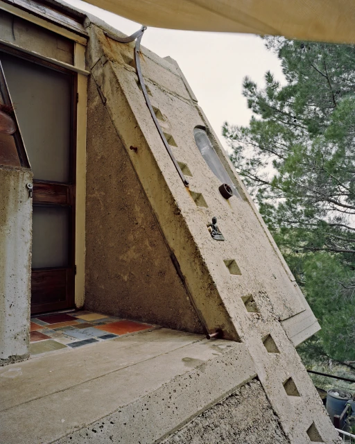 Exterior view of a concrete building with a unique architectural design, featuring a door, patterned tiles, and a textured wall.