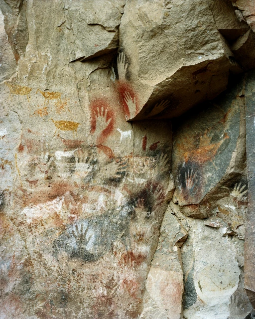 Rock wall with ancient hand paintings in red, white, black, and yellow pigment in a cave setting with rough stone texture.