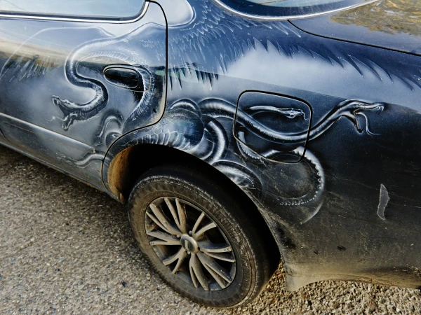 Close-up side view of a dark car featuring intricate white airbrushed dragon artwork along the rear panel and door by Derek Henderson.