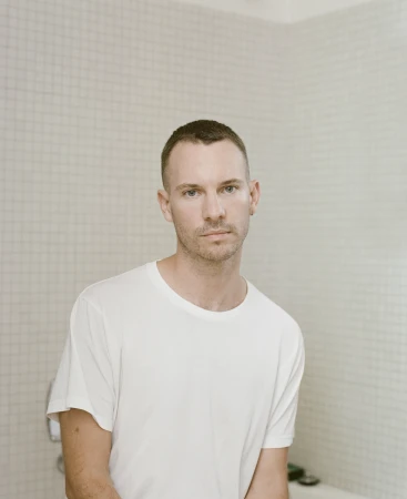 Portrait of a man in a white t shirt standing in front of a tiled wall by photographer Derek Henderson