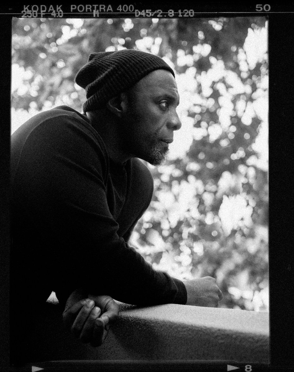 Black and white portrait of an adult male wearing a knit cap, looking off-camera in a contemplative pose, with a blurred background.
