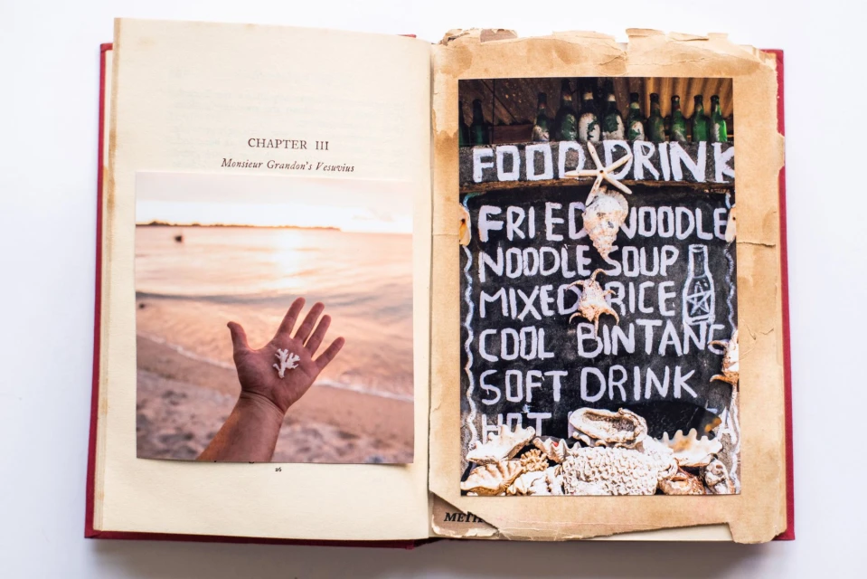 Open book featuring a photo of a hand holding coral at the beach, and another of a food and drink sign with shells.