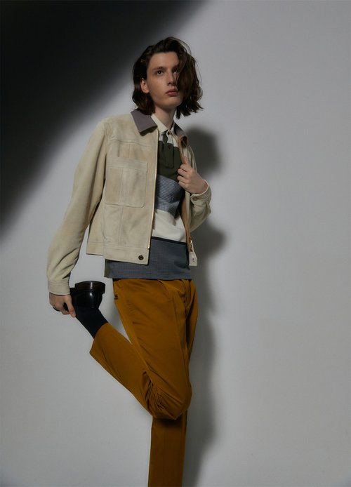 Man in stylish beige jacket and brown pants posing in a studio with shadow accentuating the outfit and creating visual interest.