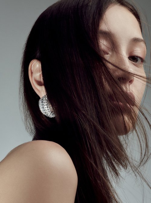 Close-up of a brunette woman with an earring, showcasing beauty and fashion. Shot in a photo studio against a solid gray background.