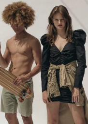 Two models posing against a white background, holding a wooden skateboard and wearing a black dress with a leopard-print jacket tied around the waist.