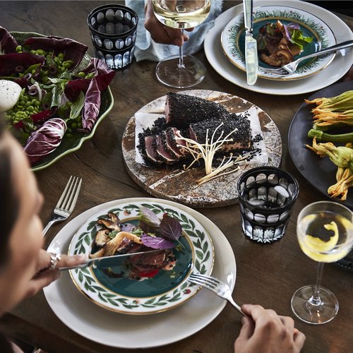 Overhead view of a dinner table laden with plates of food, including seared tuna, salad, and zucchini blossoms, accompanied by wine.