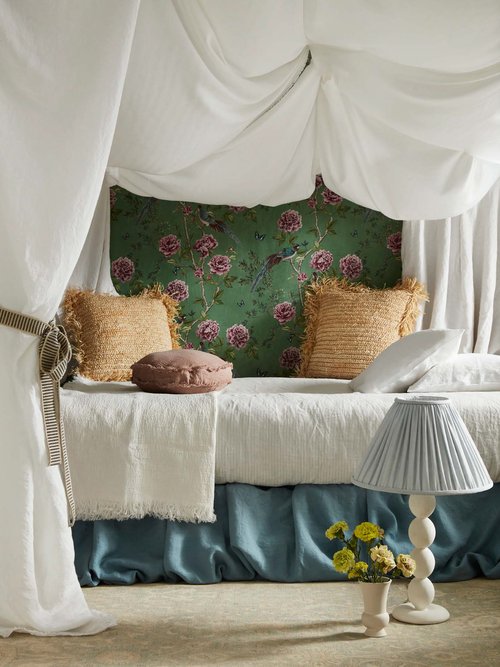 Floral patterned canopy bed in staged home interior. White and teal linen, straw pillows, and yellow flowers create a cozy, inviting space.