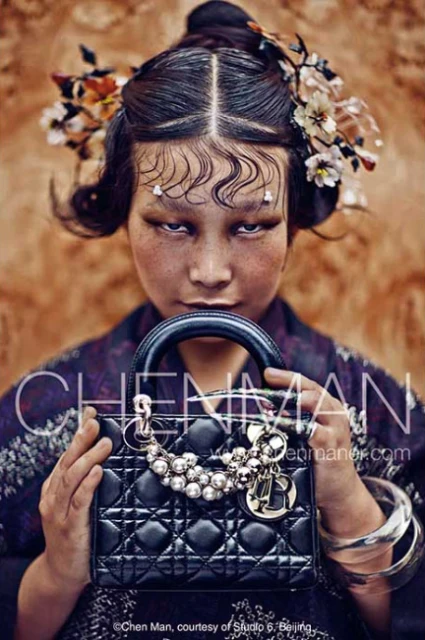 Portrait of a young Asian woman with elaborate hair and makeup, holding a black quilted handbag with silver hardware and floral decorations.
