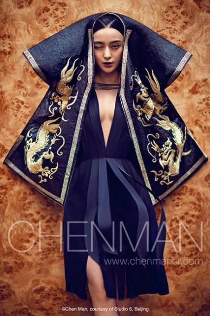An Asian woman posing dramatically in a deep V-neck dress with an embroidered cape, captured in a fashion-style shot against a wood-grain backdrop.