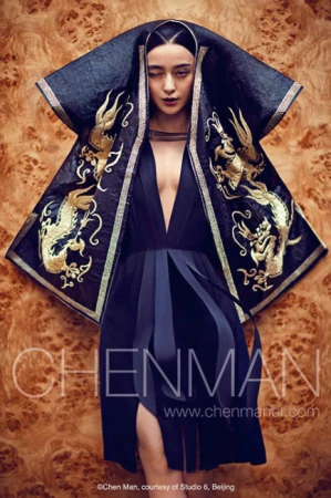 An Asian woman posing dramatically in a deep V-neck dress with an embroidered cape, captured in a fashion-style shot against a wood-grain backdrop.
