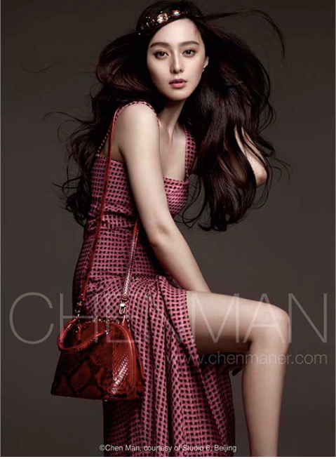Elegant woman in patterned dress with purse and jeweled headband, posing in a studio with soft lighting and a neutral backdrop.