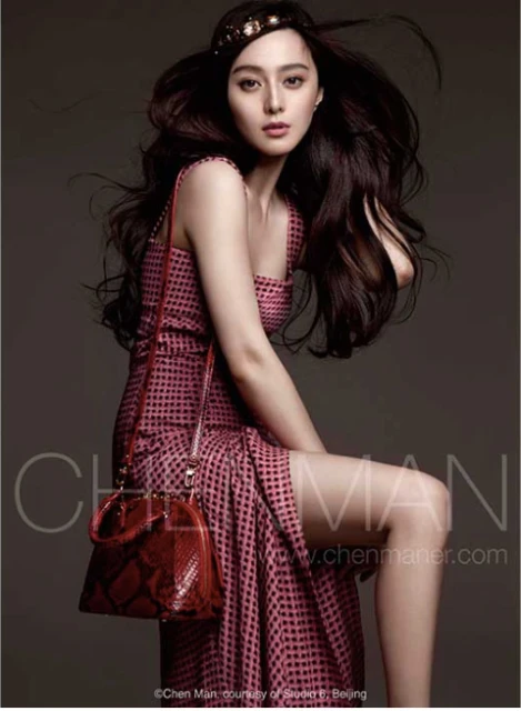 Elegant woman in patterned dress with purse and jeweled headband, posing in a studio with soft lighting and a neutral backdrop.