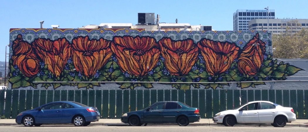 Building-side mural of orange California poppies with three parked cars below, with building facades in the background under a clear sky.