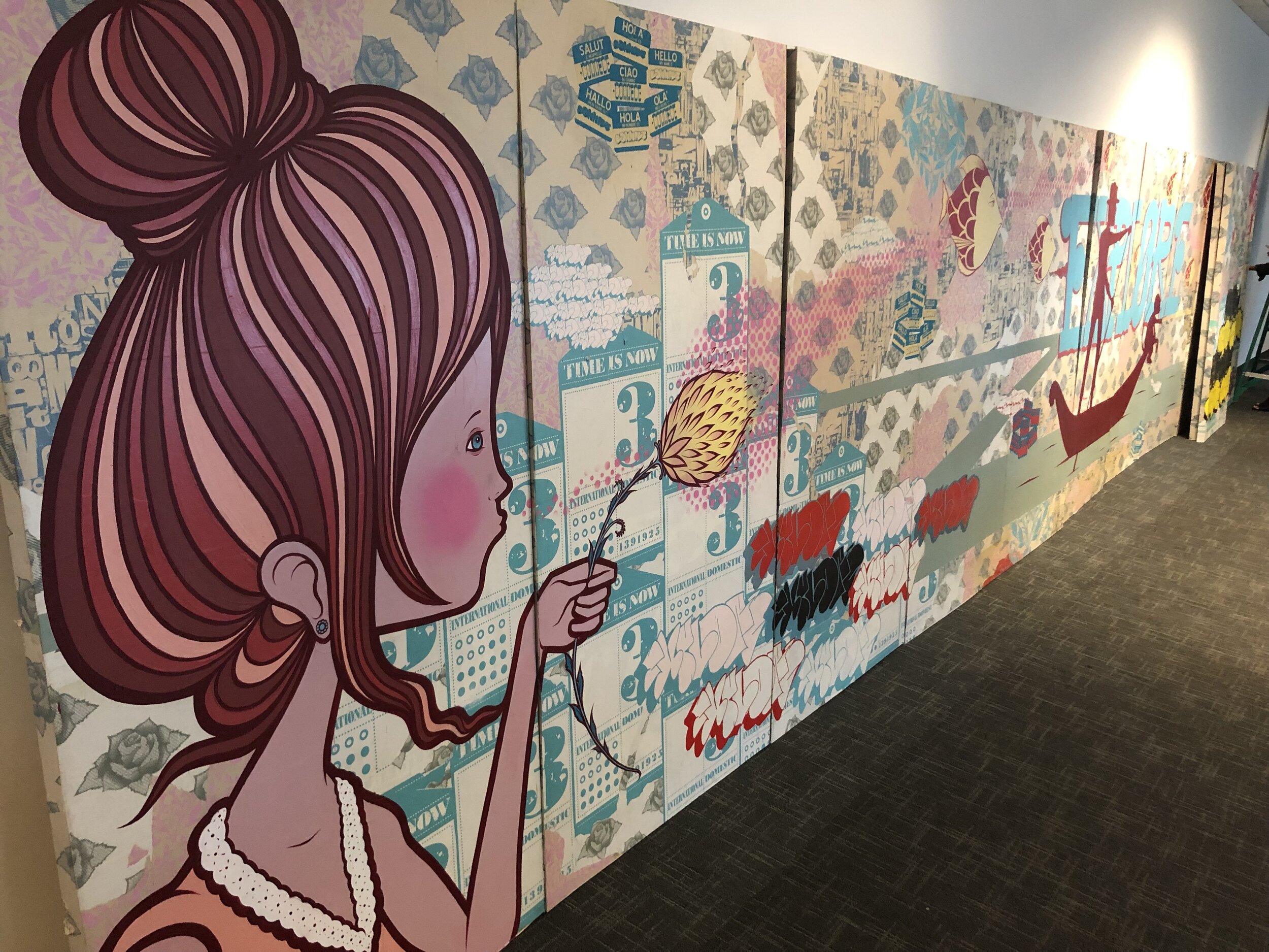 Art installation featuring a cartoon girl holding a flower against an elaborate background with text and floral patterns on multiple panels.