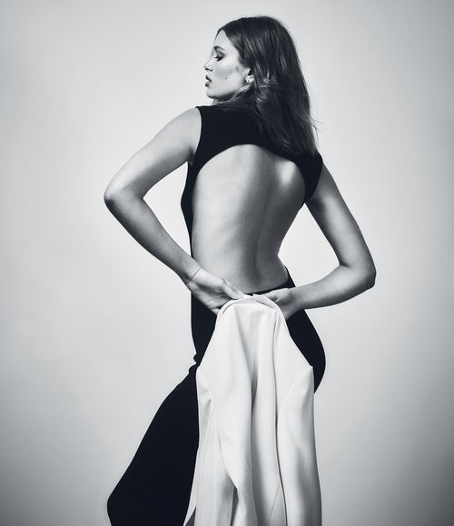 Monochrome portrait of an adult female fashion model wearing a sleeveless dress with open back, looking over her shoulder.