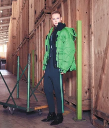 Model standing in a warehouse wearing a bright green puffer jacket and dark trousers styled by Penny McCarthy
