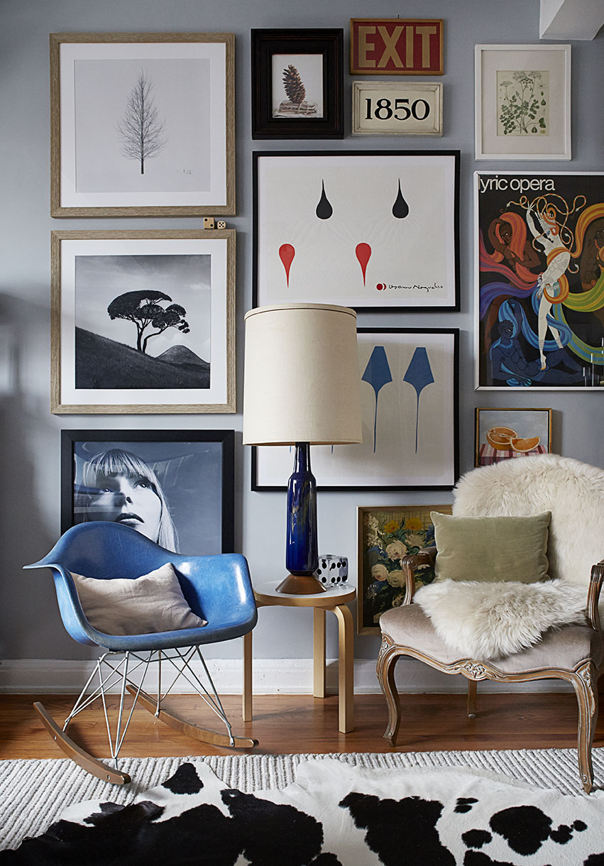 Interior view of a room with a collection of framed art on the wall above two chairs, a side table, and a patterned rug.
