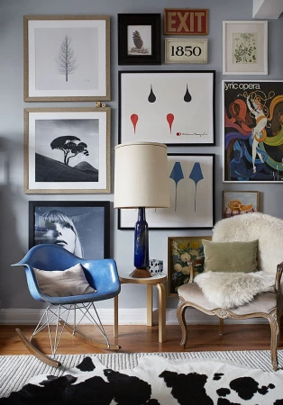 Interior view of a room with a collection of framed art on the wall above two chairs, a side table, and a patterned rug.