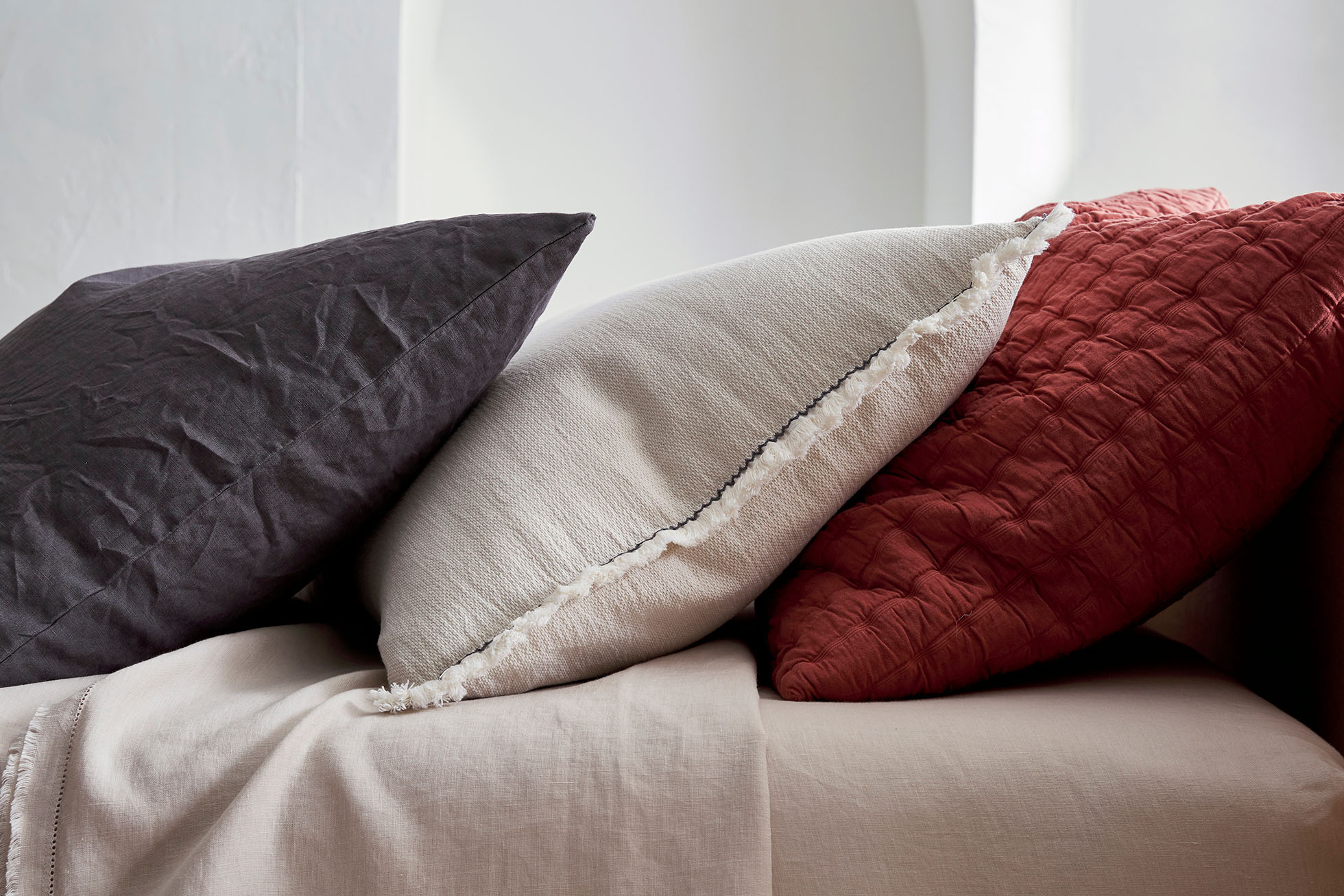 Arrangement of gray, cream, and red pillows on a bed, showcasing soft textures and neutral tones in an indoor setting.