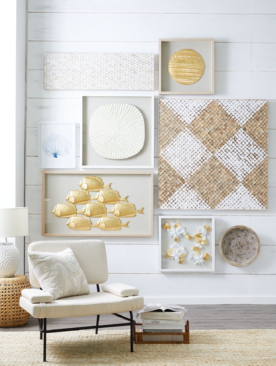 Living room interior with a white chair, woven side table, stacked books, and various framed woven art pieces on a white wall.
