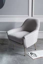 Textured grey upholstered armchair with slender brass legs on a grey floor near an open magazine