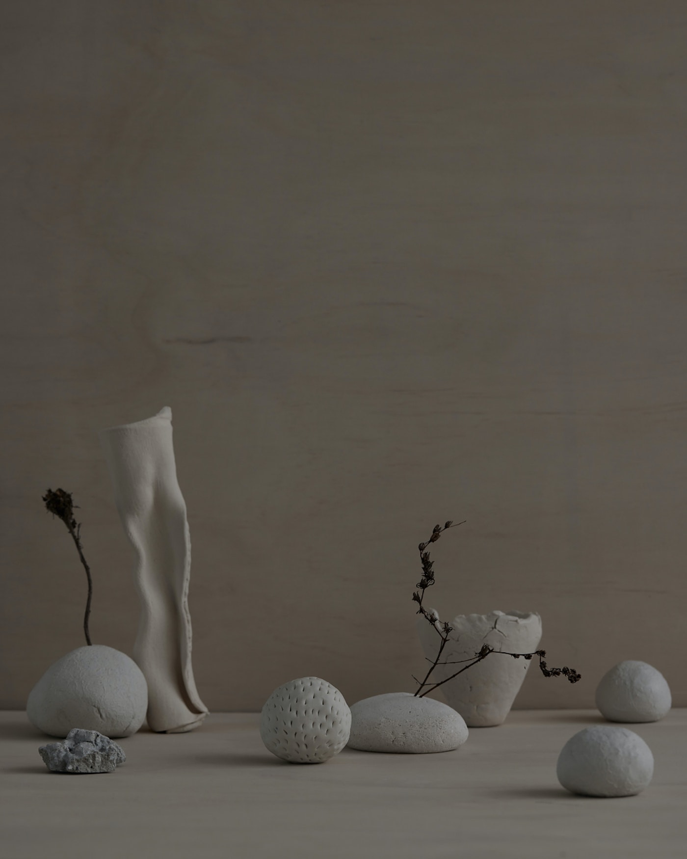Still life featuring an arrangement of white vases, ceramic spheres, and dried plants against a beige background, creating a minimalist and serene aesthetic.