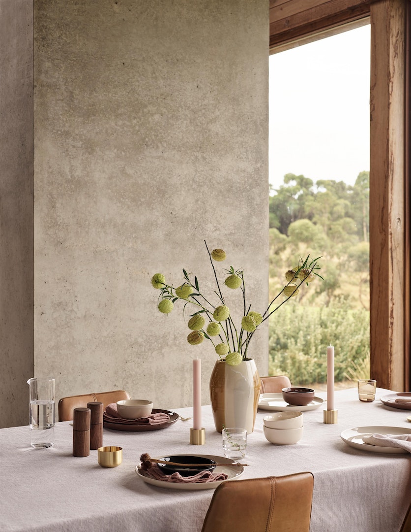 Table setting with ceramic tableware, glassware, candles, and floral arrangement, creating an elegant dining atmosphere in neutral tones.