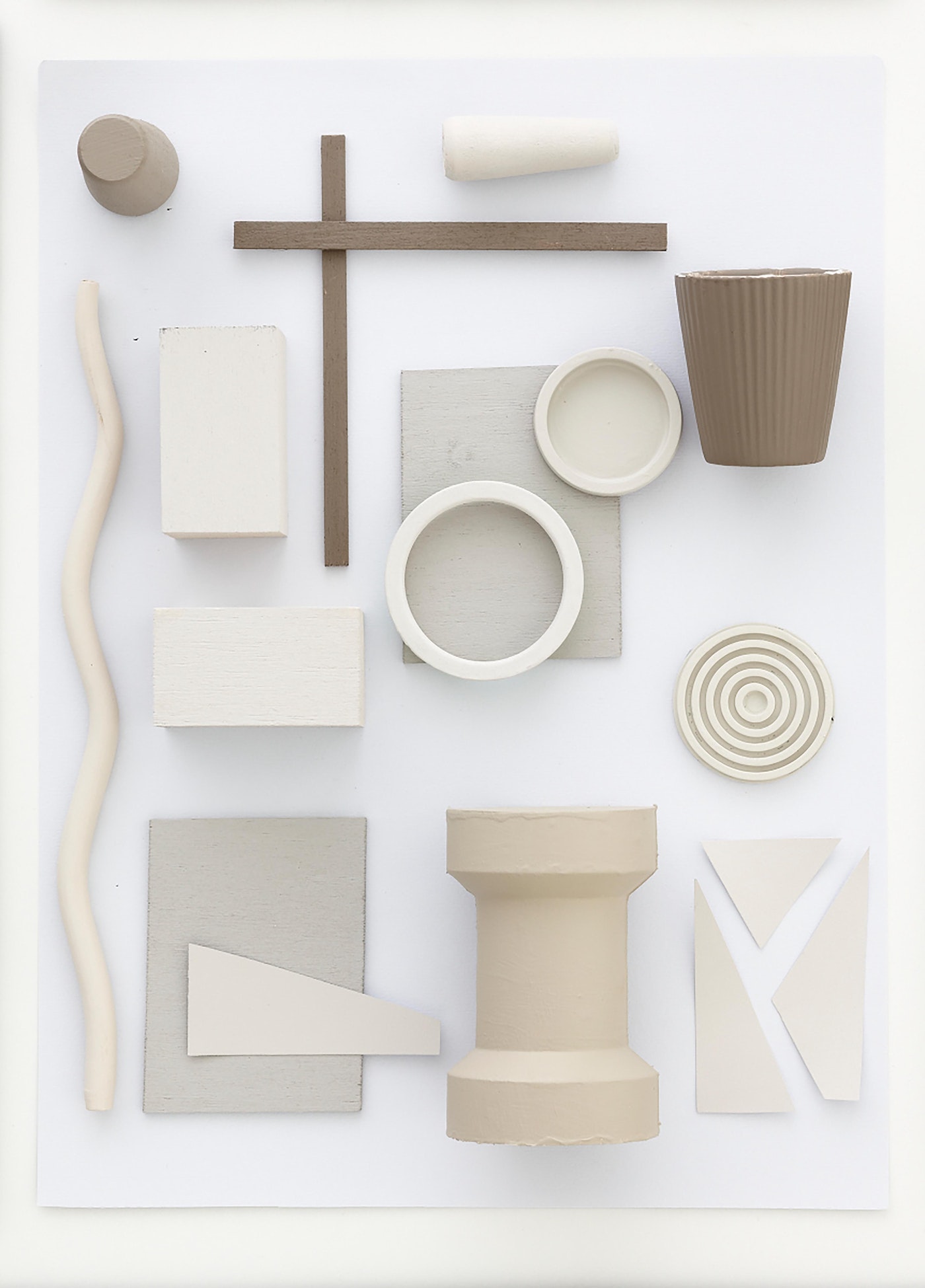 Arrangement of geometric shapes and objects in muted tones on a white background, creating a minimalist and abstract composition.