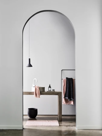 Modern bathroom interior featuring a sink, concrete vanity, black accessories, and a pink bath mat, framed by an arched doorway.