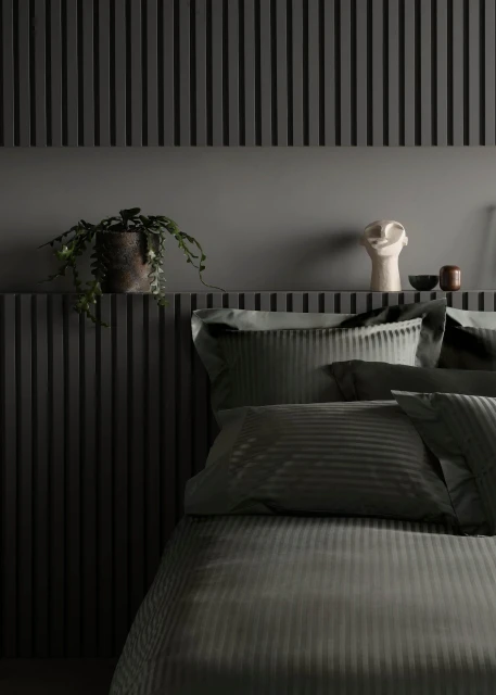 Bedroom interior with grey striped bedding, grey slatted wall paneling, potted plant, and decorative white head sculpture on shelf.
