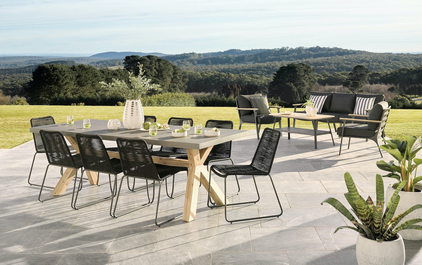 Outdoor patio dining set on stone tiles features a rectangular table with seating for ten, plus an outdoor sofa with throw pillows.