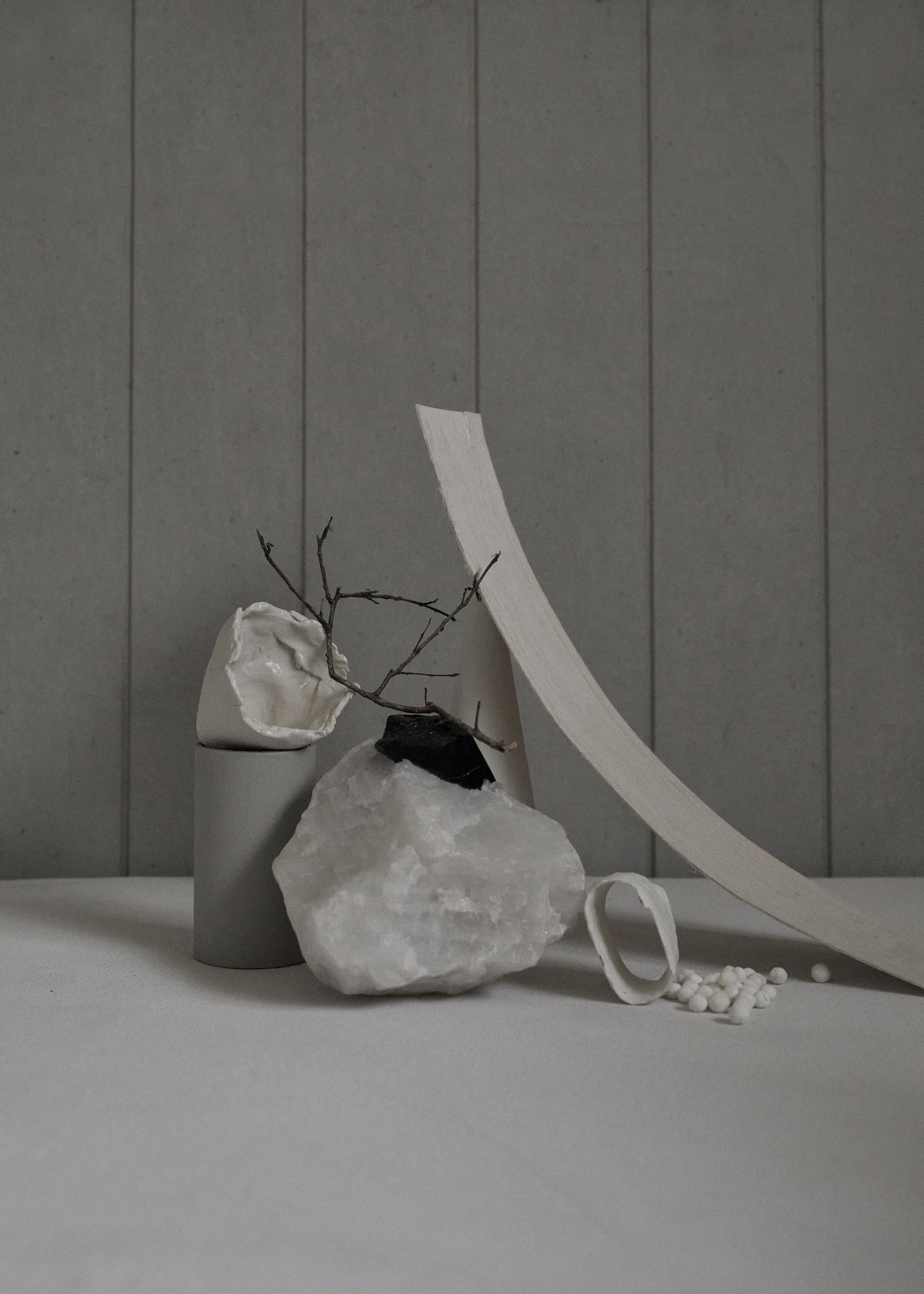 Abstract still life with rocks, branches, ceramic fragments, and neutral color palette against a simple gray backdrop for artistic visual.